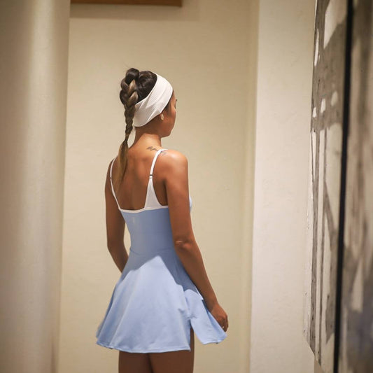

Woman in a blue dress standing in a room with a mirror.